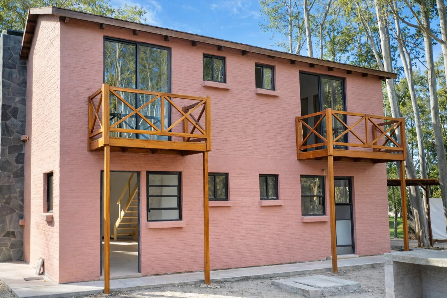 Vista frontal de una vivienda rosada con balcones de madera y terminaciones exteriores listas para entrega.