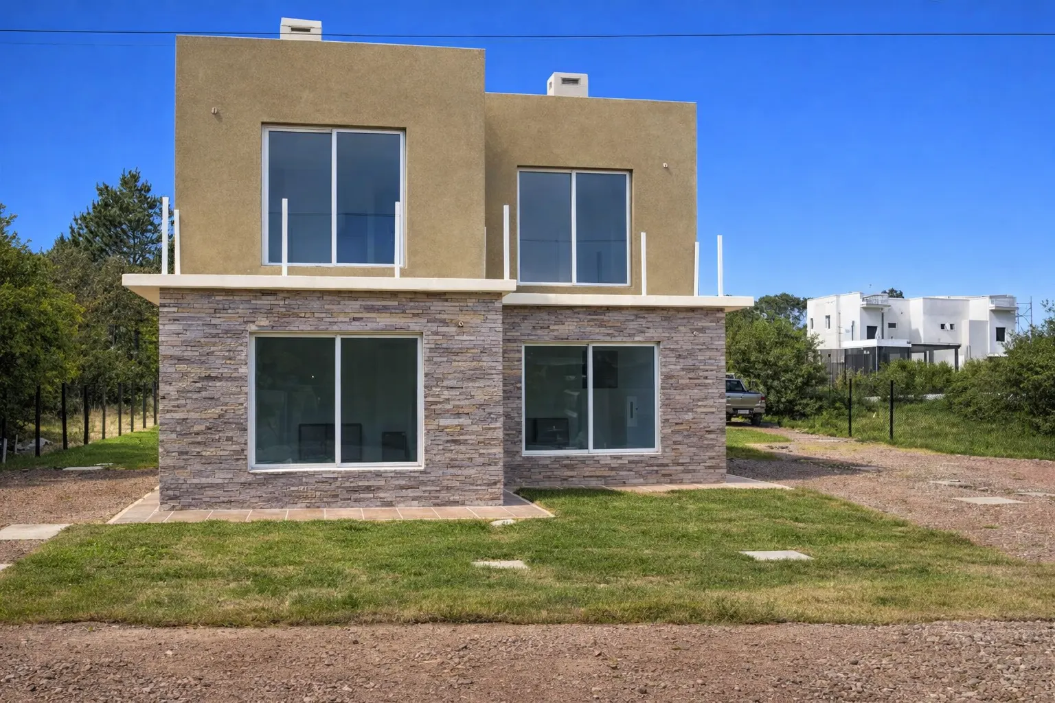 Vista frontal de vivienda de dos niveles con revestimiento símil piedra en planta baja y césped al frente.