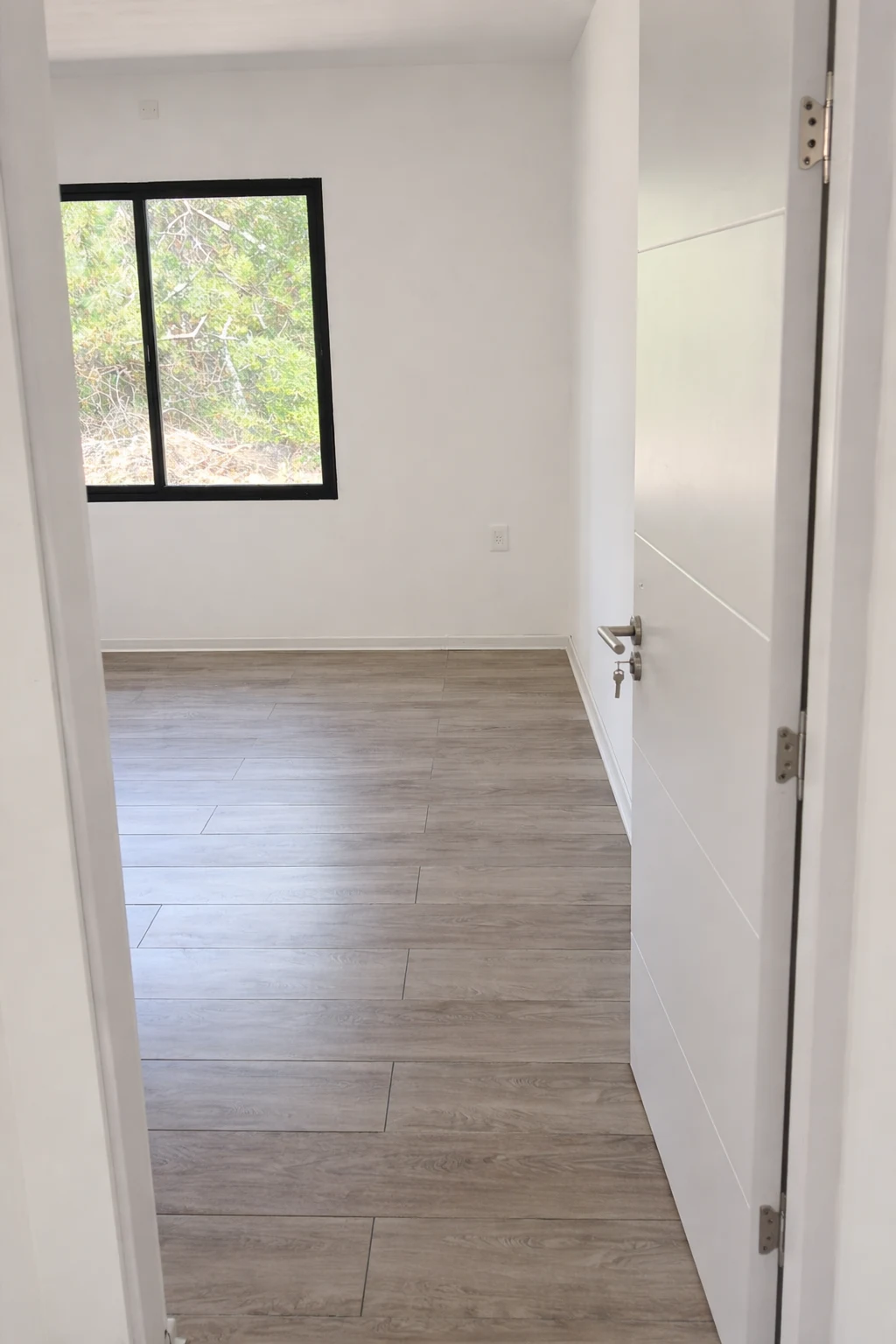 Dormitorio terminado con piso símil madera, paredes blancas y ventana negra con vista al exterior.
